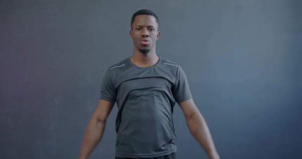 強力なアフリカ系アメリカ人スポーツマンがレジスタンスバンドで運動し 灰色の背景でカメラを見るスローモーション スポーツとアクティブライフスタイルのコンセプト — ストック動画