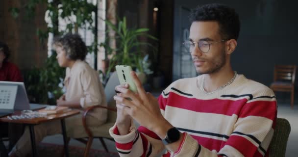 アフリカ系アメリカ人の従業員は コワーキングオフィスでスマートフォンテキストメッセージングを使用しています 最新のコミュニケーション技術とスタートアップコンセプト — ストック動画