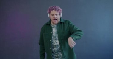 Bin yıllık tasasız dansın yavaş çekim portresi mor arka planda kulaklıklarla müzik dinlemek ve şarkı söylemek. Ses aygıtı ve modern yaşam tarzı konsepti.