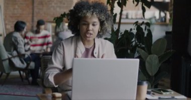 Yaratıcı kafede dizüstü bilgisayar ve kablosuz kulaklık kullanarak online video görüşmesi yapan Afrikalı Amerikalı bir kadın. Serbest meslek ve uzaktan iletişim kavramı.