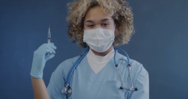 Üniformalı Afrikalı Amerikalı doktorun yavaş çekimde portresi mavi arka planda enjeksiyona hazır. İlaç ve aşı kavramı.