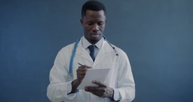 Reçete yazan Afro-Amerikan doktorların portresi. Sonra kameraya bakıp gri arka plan üzerine ödev veriyor. Tıp ve sağlık hizmetleri kavramı.