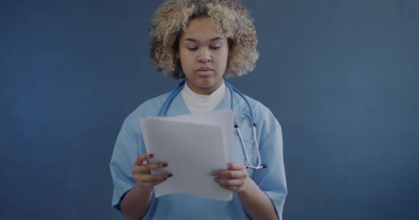 Portret Afroamerykańskiego Lekarza Czytającego Dokumentację Medyczną Dokumenty Stojące Niebieskim Tle — Wideo stockowe