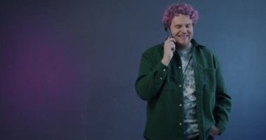 Cep telefonuyla konuşan genç adamın yavaş çekim portresi gülümseyip mor arka planda öfkesini dile getiriyor.