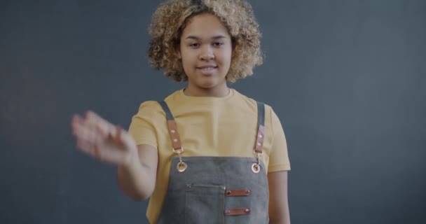 エプロンの起業家のアフリカ系アメリカ人の女性のゆっくりとした動きの肖像画は Okの手のジェスチャーを示し 灰色の背景にウインクします 中小企業と成功者コンセプト — ストック動画