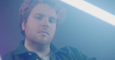 Parlayan neon lambalarla eskrim yapan adamın yakın plan portresi mor arka planda duman bulutları arasında. Siber punk ve aydınlatma kavramı.