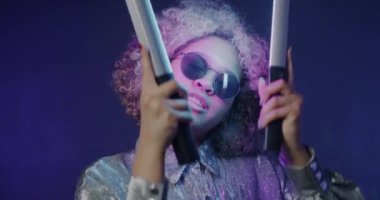 Mavi arka planda neon lambalarla dans eden havalı Afrikalı Amerikalı kızın yavaş çekim portresi. Parti ve kutlama konsepti.