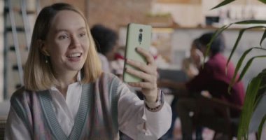 Sanal toplantı sırasında iş konuşan serbest çalışan bir kadın iş yerinde akıllı telefonla online video görüşmesi yapıyor. Serbest meslek ve modern teknoloji konsepti.