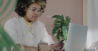 İnternet üzerinden alışveriş yapan mutlu Afro-Amerikalı kız dairede gülen dizüstü bilgisayarla kredi kartıyla ödeme yapıyor. Bankacılık ve tüketim kavramı.
