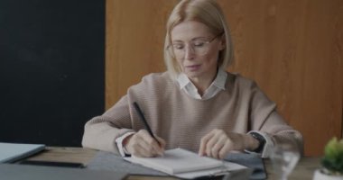 Düşünceli olgun bir kadının portresi notlar yazıyor sonra kameraya bakıyor ve modern ofisin içinde gülümsüyor. İş kadını ve psikoloji konsepti.