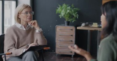 Olgun kadın psikolog, kadın müşteriyle konuşuyor. Yazan kadını dinliyor. Ofiste notlar alıyor. İnsanlar ve terapi konsepti.