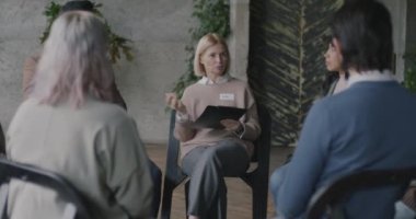 Profesyonel terapist bir grup insanla konuşuyor ve notlar alıyor. Çember halinde oturup destek verme sorunları yaşıyorlar. Psikoloji ve akıl sağlığı kavramı.