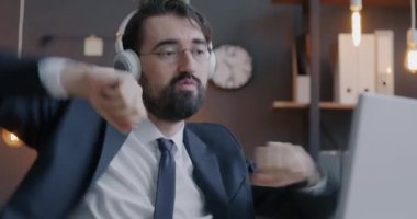 Orta Doğulu yaratıcı işadamlarının kablosuz kulaklıklarla müzik dinlemesi ve dans etmesi akşamları bilgisayar masasında oturması.