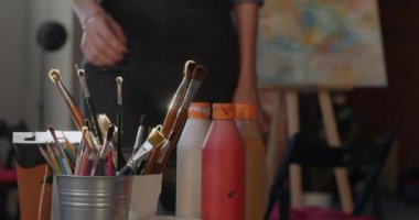 Kadın elinin boya fırçasıyla yavaş çekimde, sonra kadın ressam stüdyoda resim yapmakla meşgul olarak sehpada yürüyor. Güzel sanatlar ve insanlar konsepti.