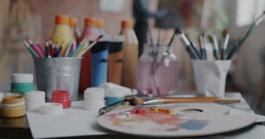 Resim aletlerinin yakın çekimleri kalem paleti fırçaları ve renkli boyalarla stüdyo arka planında çalışan bulanık ressamlar. Yaratıcı meslek ve güzel sanatlar konsepti.