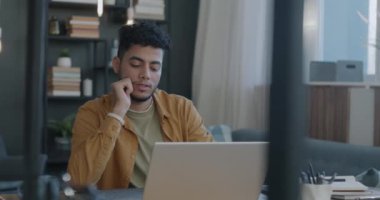Aydınlatılmış dairede dizüstü bilgisayarla çalışan Arap bir adamın ağır çekimde çalışması. Modern teknoloji ve profesyonel işgal kavramı.