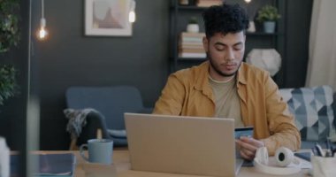 Diz üstü bilgisayar ve kredi kartı kullanan neşeli bir Arap bankacılık uygulaması ve evde online alışveriş yapmaktan mutlu oluyor. Finans ve modern teknoloji kavramı.