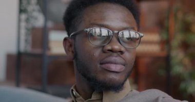 Düşünceli Afro-Amerikan bir adamın yakın plan portresi kameraya dönüp gülümseyerek evde olumlu duygular ifade ediyor. Halk ve yerli yaşam tarzı kavramı.