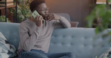 Afro-Amerikalı biri cep telefonuyla konuşuyor. Kanepede oturmuş haberleri tartışıyor. Yaşam tarzı ve iletişim konsepti.