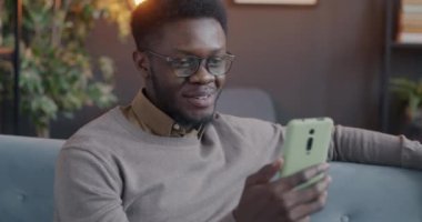 Neşeli Afro-Amerikalı bir adam akşam evde akıllı telefon kullanarak çevrimiçi video konuşması yapıyor. İnsanlar ve internet iletişim kavramı.