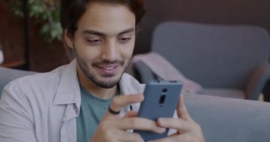 Orta Doğulu bir adamın akıllı telefon kullanması ve evde sosyal medyanın keyfini sürerken ekrana bakıp gülmesi. Gadget ve insanlar konsepti.