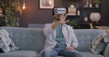 Sanal gerçeklik gözlüğü takan genç adam akşam evde oyundan zevk alırken el sıkışıyor. Eğlence ve modern teknoloji konsepti.