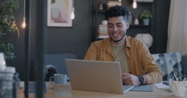 Neşeli Orta Doğulu adam evde el sallayarak dizüstü bilgisayarla video görüşmesi yapıyor. İletişim ve insan kavramı.