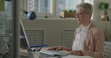 Olgun iş kadını internette bilgisayar ve kulaklıkla el hareketini gösteren bir video görüşmesi yapıyor. İletişim ve başarılı iş kavramı.