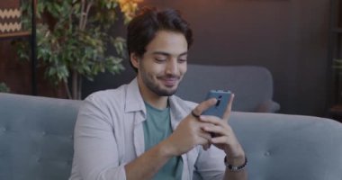 Akıllı telefon kullanan mutlu Arap öğrenci akşamları apartmanda otururken internet içeriğinin keyfini çıkarıyor. Gadget ve milenyum konsepti.