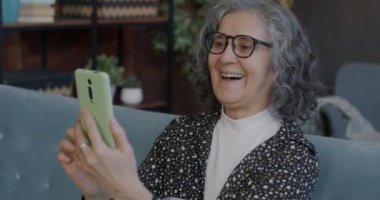 İnternetten konuşan mutlu son sınıf kızının portresi. Evde akıllı telefon kullanarak gülerek sohbetten keyif alıyor. İletişim ve yaşlılar konsepti.