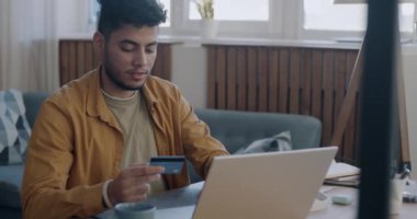 Kredi kartı ve dizüstü bilgisayar kullanan neşeli bir Arap evde bankacılık uygulamasından memnun gülümsüyor. Finans ve para kavramı.