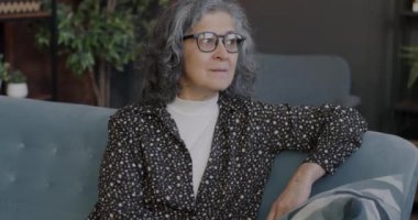 Dairedeki koltukta oturmuş kameraya gülümseyen yaşlı kadının yavaş çekim portresi. Emekli insan ve aile hayatı kavramı.