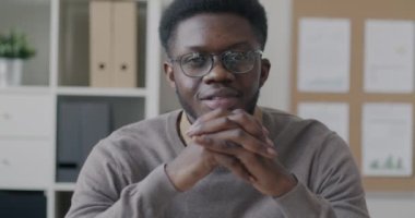 Ofiste oturmuş kameraya gülümseyen neşeli Afrikalı Amerikalı yöneticinin yavaş çekim portresi. Halk ve iş kavramı.
