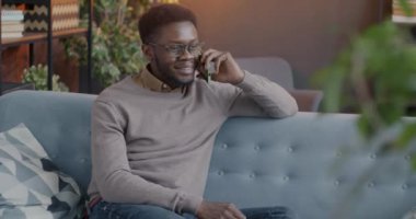 Cep telefonuyla konuşan Afro-Amerikalı adam koltukta oturup gülümseyen ve evde keyifli sohbetler yapan. İnsanlar ve cep telefonu iletişim kavramı.