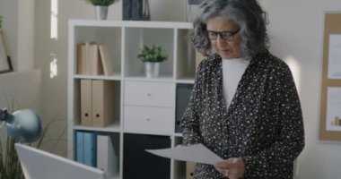 Yaşlı iş kadını belge okuyor ve ofiste çalışan bilgisayar ekranı bilgilerine bakıyor. Kariyer ve iş konsepti.