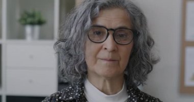 Ofiste ciddi bir yüzle kameraya bakan deneyimli bir iş kadınının yavaş çekim portresi. İş ve yaşlılar konsepti.