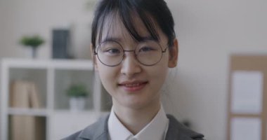 Hafif ofisteki kameraya gülümseyen Asyalı genç bayanın yavaş çekim portresi. Başarılı insanlar ve iş konsepti.