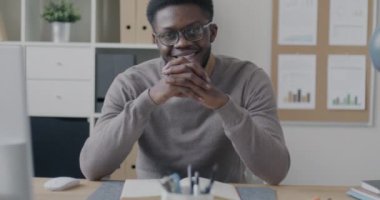 Ofiste oturmuş kameraya bakarak gülümseyen başarılı Afrikalı Amerikalı iş adamının yavaş çekim portresi. İş ve finans kavramı.