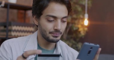 Mutlu bir Arap, internet üzerinden akıllı telefon alışverişini kredi kartıyla yapıyor ve gülümsüyor ve modern teknolojinin keyfini çıkarıyor. Tüketim ve insan kavramı.