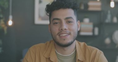 Akşamları aydınlık bir dairede kameraya gülümseyen yakışıklı Orta Doğulu adamın yavaş çekim portresi. İnsanlar ve ev kavramı.