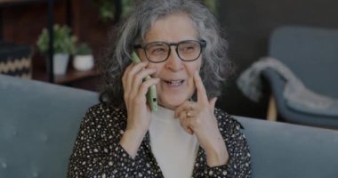 Neşeli, son sınıf öğrencisi bir kadın cep telefonuyla konuşuyor. Evde el hareketlerini gösteriyor. Yaşlılar ve cep telefonu iletişim kavramı.