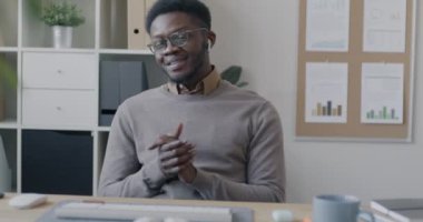 Afrika kökenli Amerikalı bir çalışanın kablosuz kulaklıkla kameraya bakıp ofiste konuşurken çekilmiş bir portresi. İş ve iletişim kavramı.