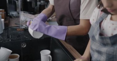Ellerinizi lastik eldivenlerle kapayın. Bulaşıkları yıkayın. Çocuklar da tabakları ve fincanları silsin. Ev işleri ve aile hayatı konsepti.