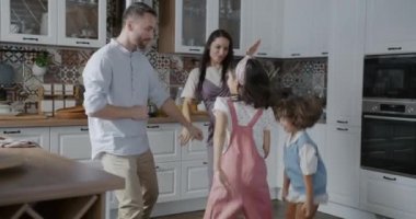 Neşeli insanlar, ebeveynler ve çocuklar evde dans edip mutfaktaki müzikten zevk alıyorlar. Aile ilişkisi ve boş zaman konsepti.