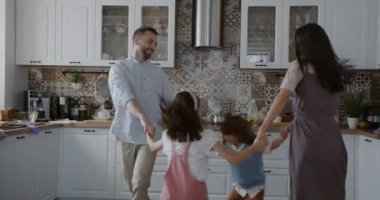 Tasasız ebeveynler ve çocuklar evde el ele dans edip eğleniyorlar. Mutlu aile ve aktif yaşam tarzı kavramı.