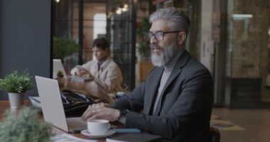 Laptop bilgisayar kullanan deneyimli bir iş adamı. Sonra kafede çalışan cep telefonuna cevap veriyor. Profesyonel iletişim ve iş konsepti.