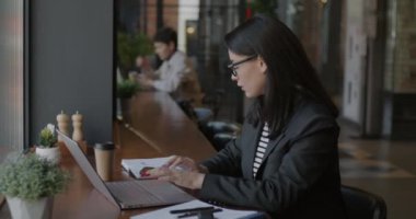 Başarılı genç iş kadını cep telefonuyla konuşuyor ve kafede dizüstü bilgisayarla çalışıyor. Modern teknoloji ve hırslı girişimci konsepti.
