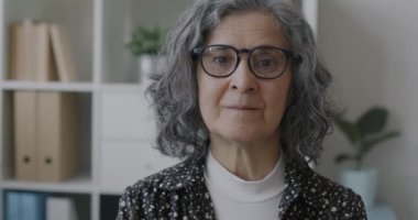 İş yerindeki kameraya bakan yaşlı, kendine güvenen bir iş kadınının yavaş çekim portresi. İş ve deneyimli çalışan kavramı.