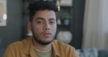 Evin arka planındaki bulanık kameraya bakan dalgın bir Arap 'ın yavaş çekim portresi. İnsanlar ve duygu kavramı.