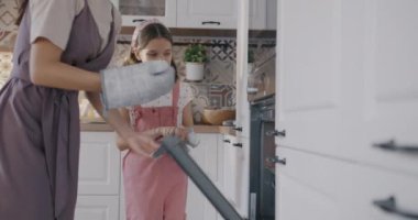 Genç bir kadın ve kız bisküvi pişiriyor fırından yemek çıkarıyor ve evde birlikte yemek pişiriyorlar. Aile ve aşçılık kavramı.